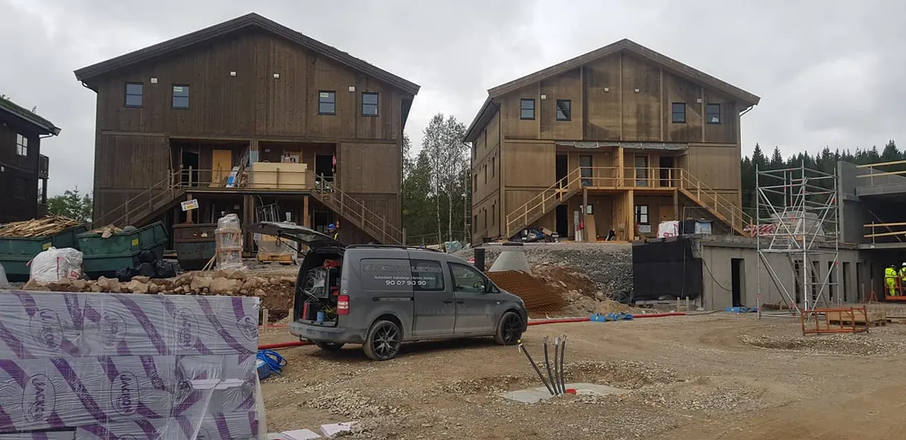 To tømmerhus under oppføring med en firmabil parkert foran
