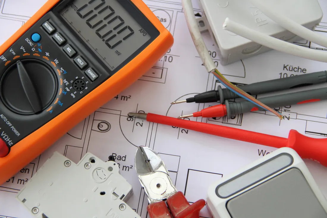 Et multimeter, en automatsikring og skrutrekkere liggende på en elektrisk plantegning